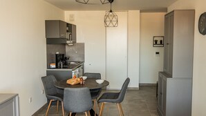 A compact kitchen with grey cabinets, a dining table with four chairs, and a hanging light fixture. - Confortable T2 avec terrasse, parking & vue étang (Sète)