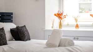 En pænt redt seng med dekorative puder, et vindue med udsigt og en vase med blomster på vindueskarmen.