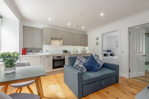 A modern kitchen with grey cabinets, a built-in oven, and a dining area with a grey table and chairs.