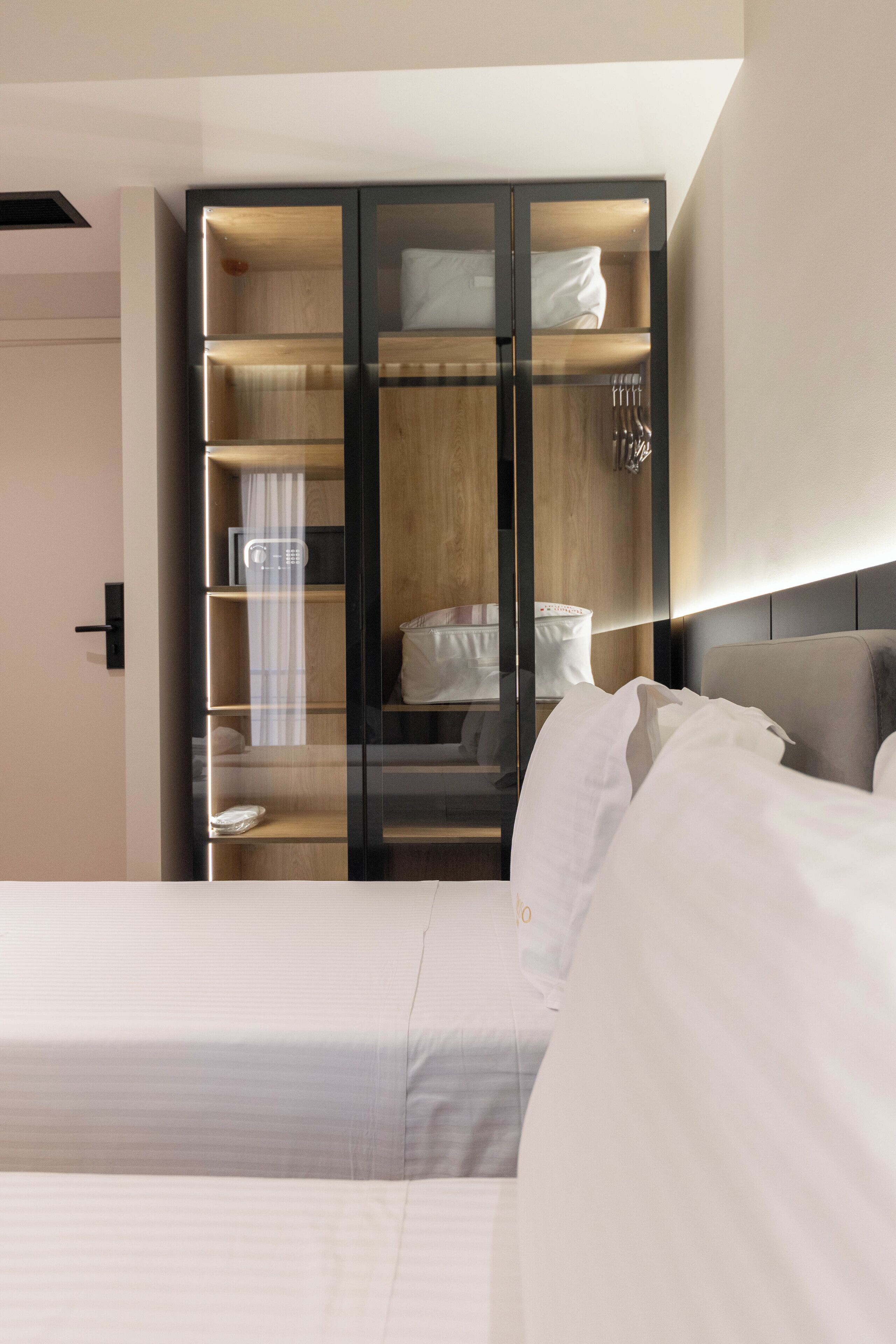 Una habitación de hotel moderna con una cama grande, un armario empotrado con varios estantes y una mesita de noche.