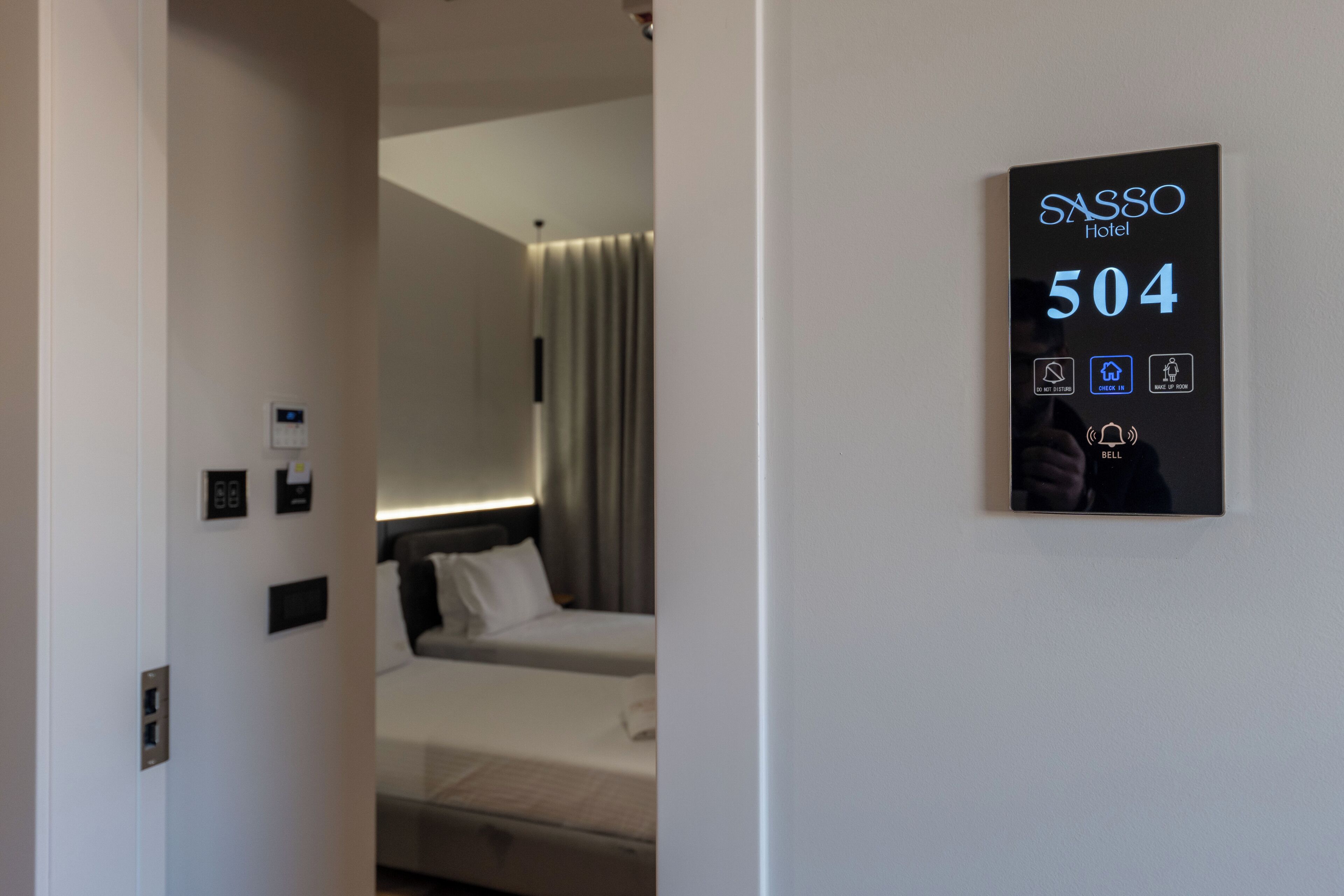 A hotel room with a bed, a wall-mounted control panel displaying room number 504, and a door with a handle.