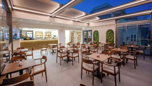 A spacious indoor dining area with wooden tables and chairs, a bar area with a counter, and large windows providing natural light. - Sasso Hotel (Vlorë)