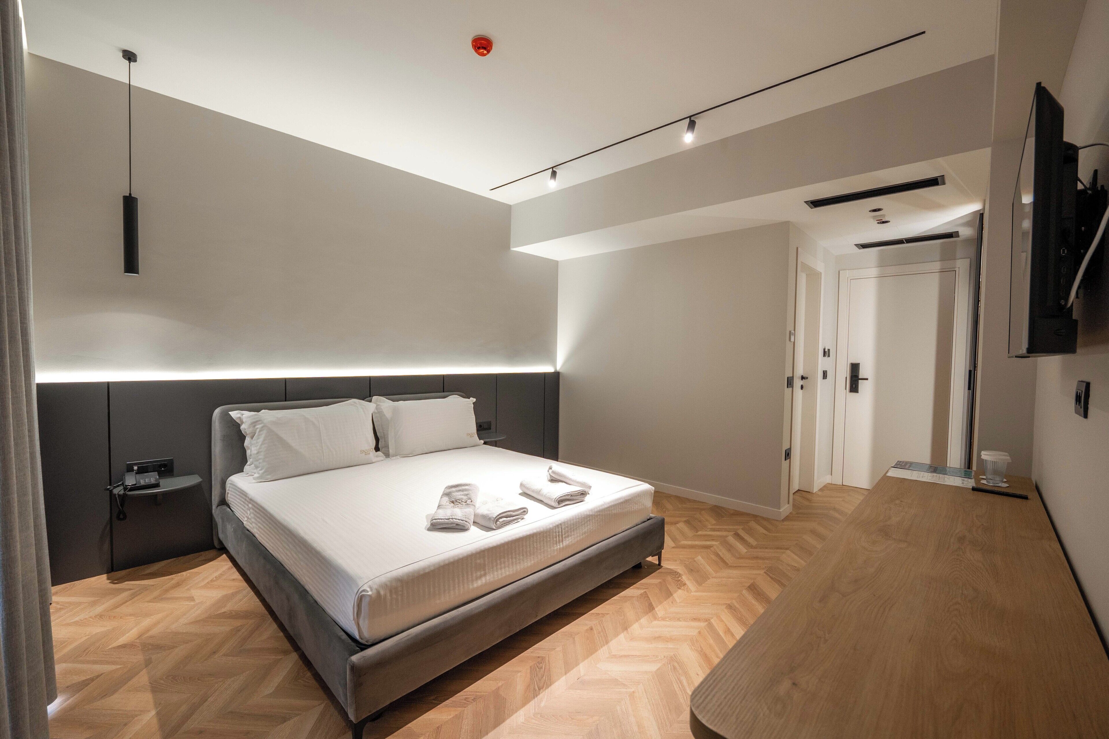 Un dormitorio moderno con una cama grande, mesitas de noche, un televisor y suelo de madera.