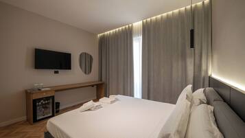 Une chambre d’hôtel moderne dotée d’un grand lit, d’un téléviseur à écran plat fixé au mur, d’un minibar et d’une grande fenêtre avec des rideaux.