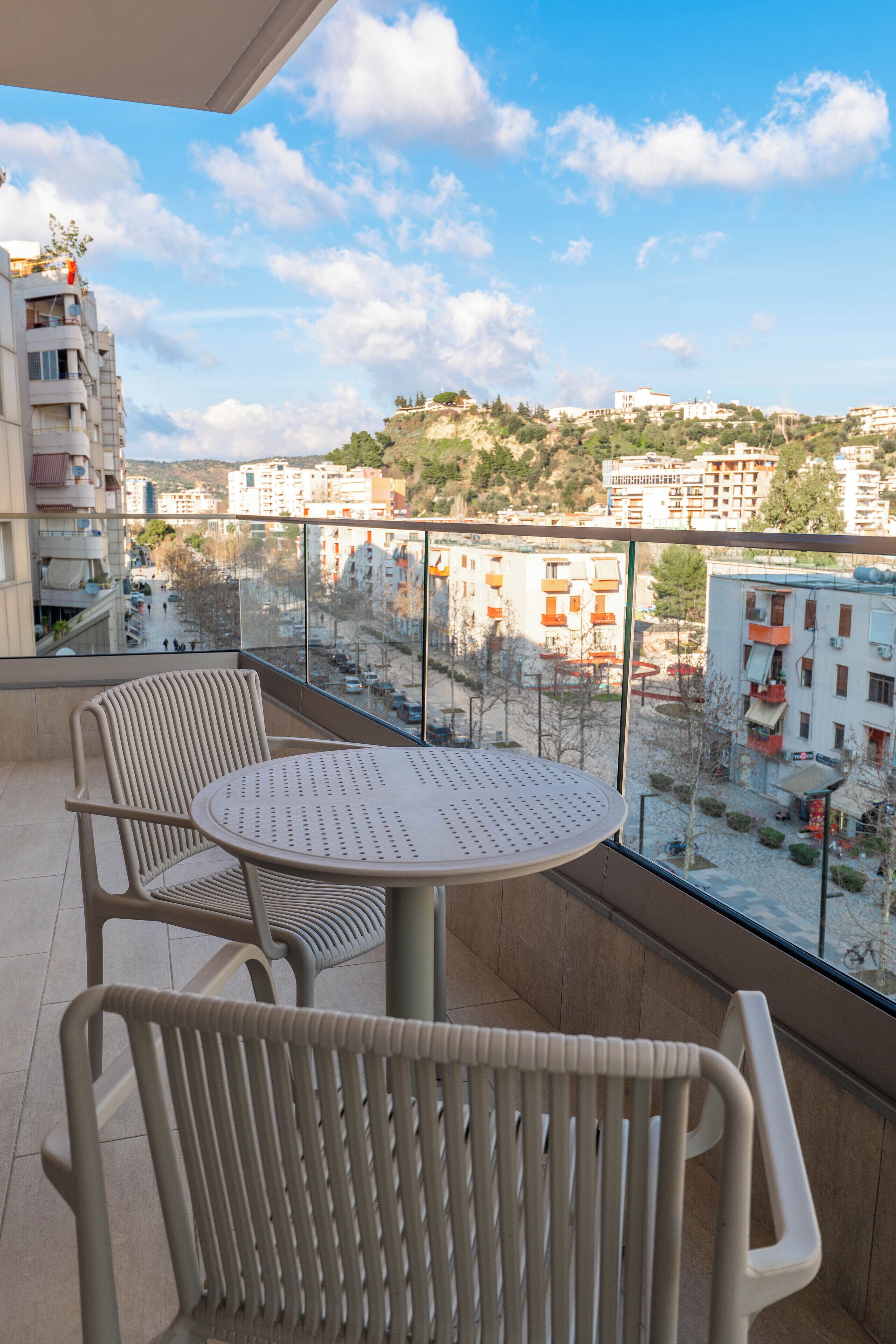 A balcony with a table and chairs, offering a view of a cityscape with buildings and trees.