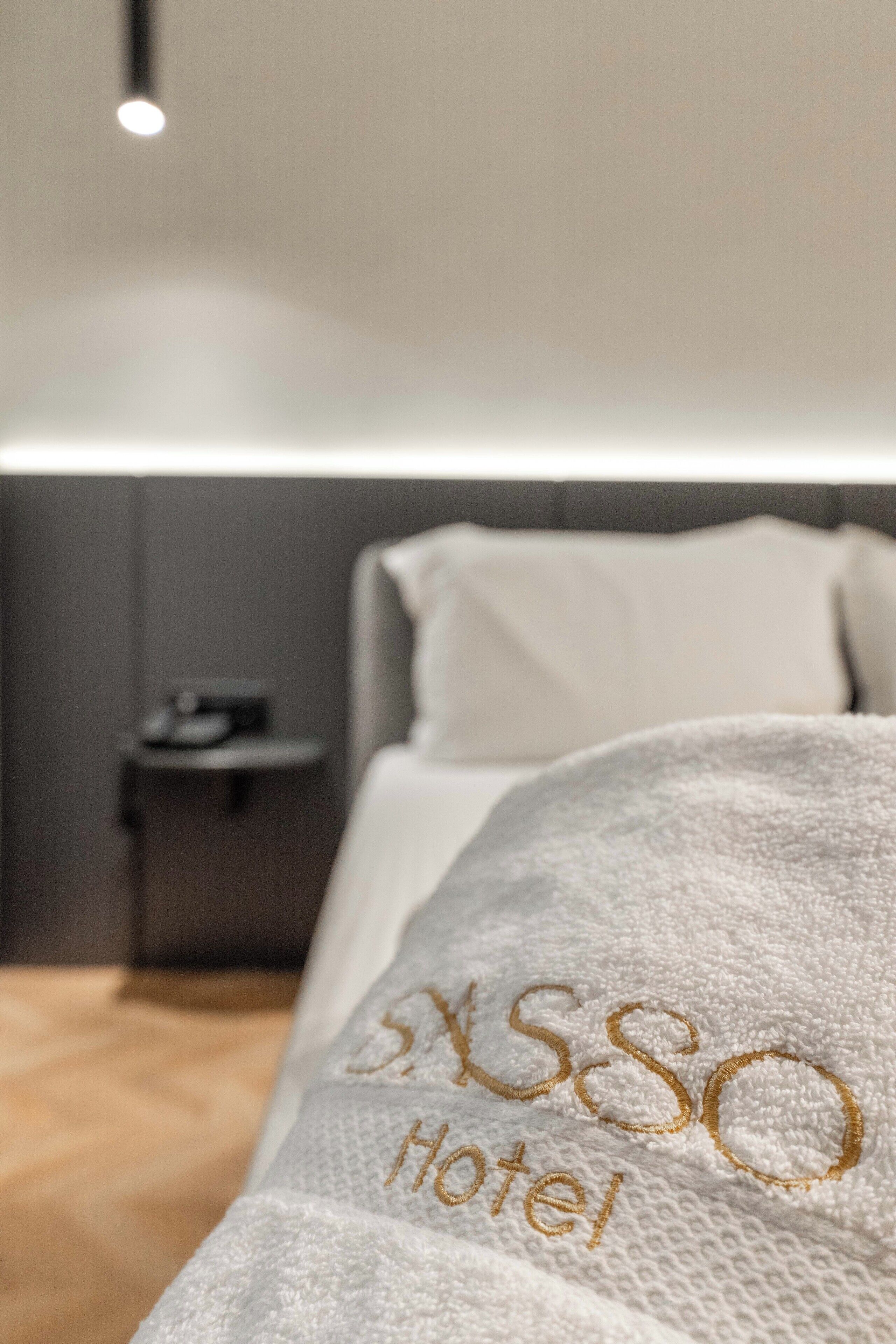 A hotel room with a neatly made bed, a bedside table, and a wall-mounted light.