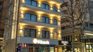 A multi-story hotel with illuminated signage, a parked car, and a visible storefront. - Sasso Hotel (Vlorë)