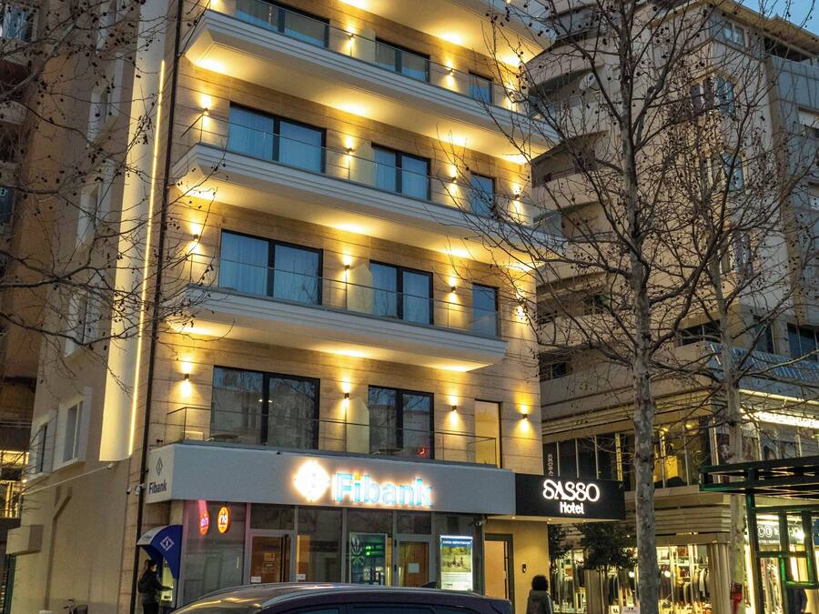 Et hotel med flere etager, oplyst skiltning, en parkeret bil og en synlig butiksfacade.