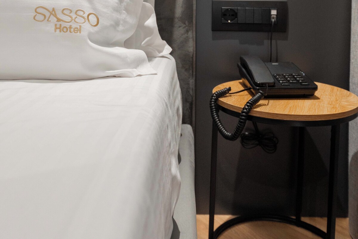Una habitación de hotel con una cama, una mesita de noche con teléfono y un enchufe.