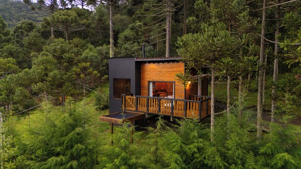A cabin with a wooden deck and a small porch, surrounded by dense forest. - Cascata dos Amores (Urubici)