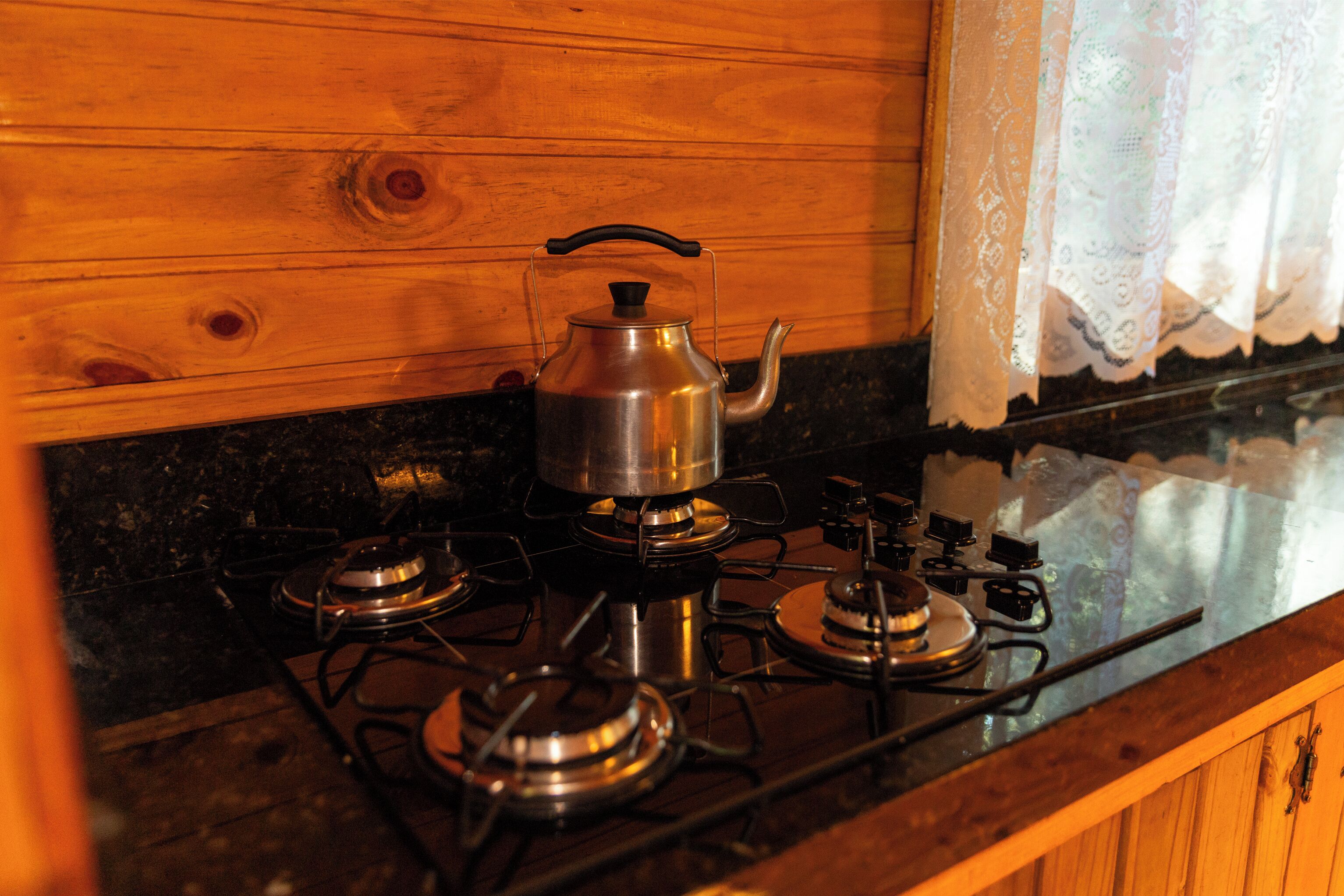 A kitchen with a gas stove, a kettle, and a wooden wall.