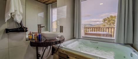 Un baño con tocador de madera, una bañera grande, un lavabo y una ventana con vistas a un balcón y montañas.