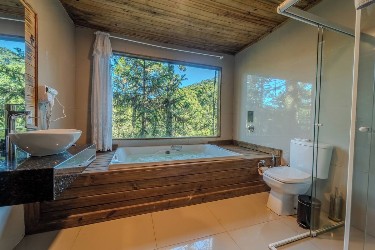 Une salle de bain moderne dotée d’une grande fenêtre, d’une baignoire, de toilettes et d’un espace douche.
