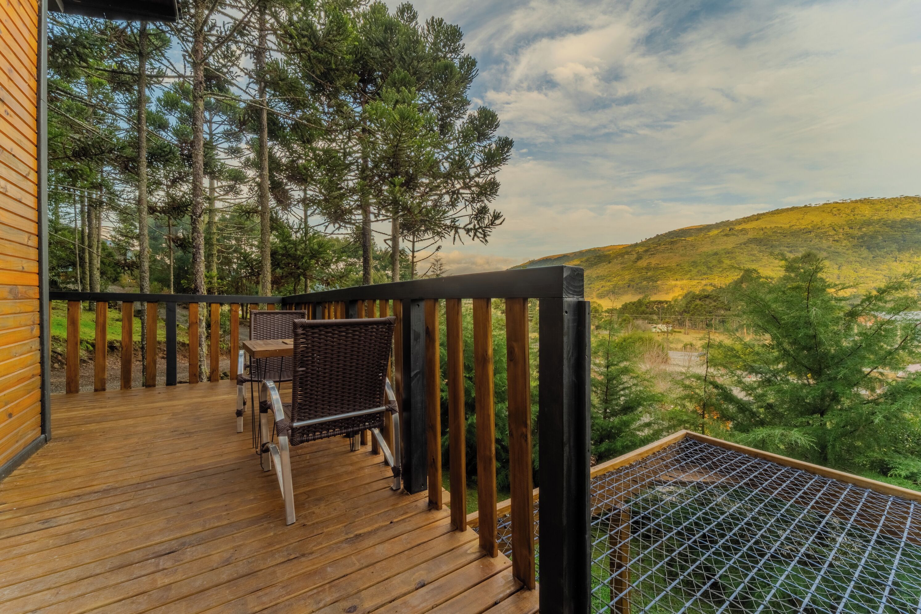 A wooden deck with a wicker chair and table, overlooking a forested hillside.