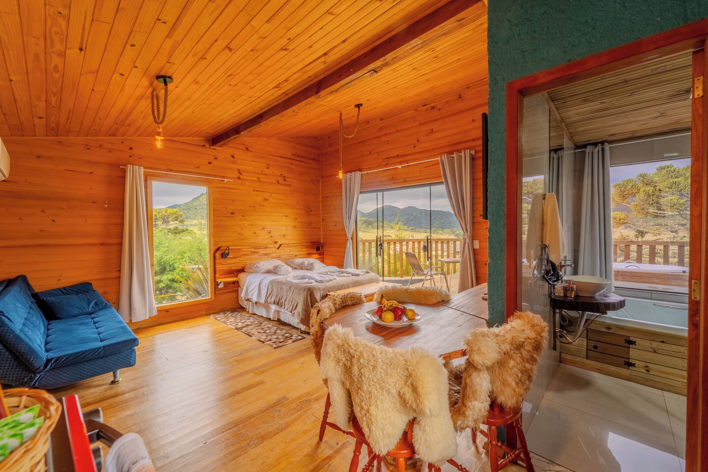 Una cabaña de madera con comedor, sofá y cama con vistas a las montañas.