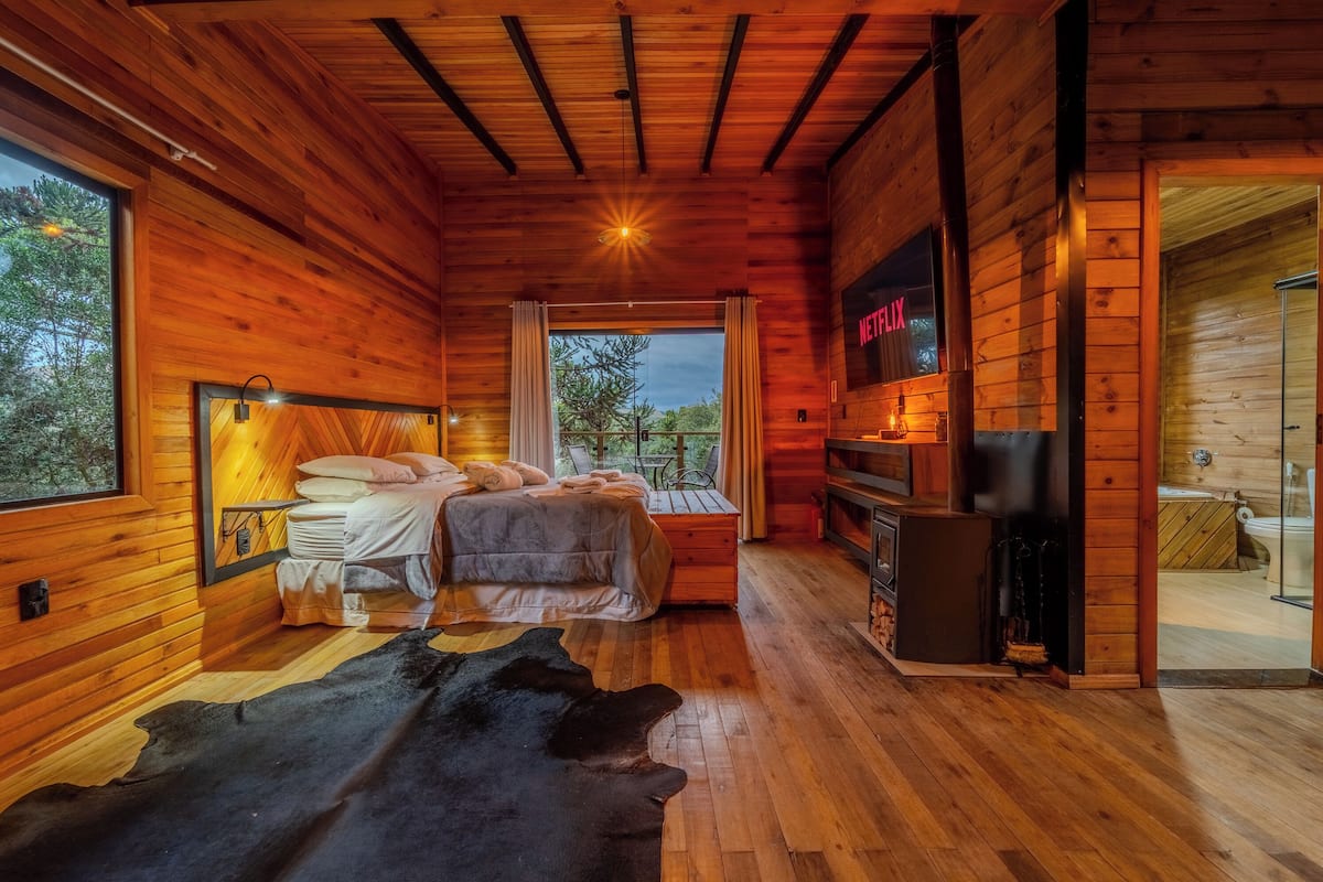 Un chalet confortable avec un intérieur en bois, un lit avec des oreillers, une télévision et une cheminée.