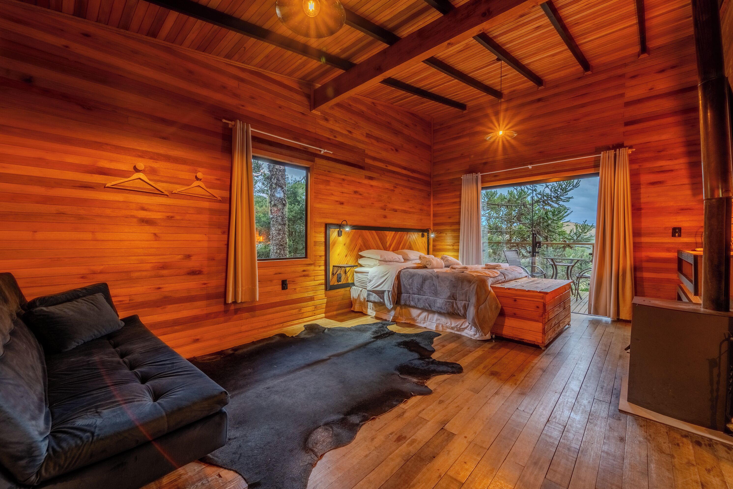 Un chalet confortable avec un intérieur en bois, un lit, un canapé et une grande fenêtre donnant sur le paysage extérieur.