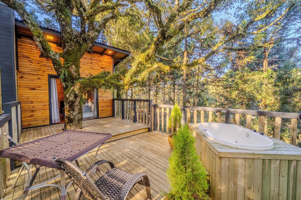 Une terrasse en bois avec un jacuzzi, des fauteuils en osier et une vue sur une zone boisée.