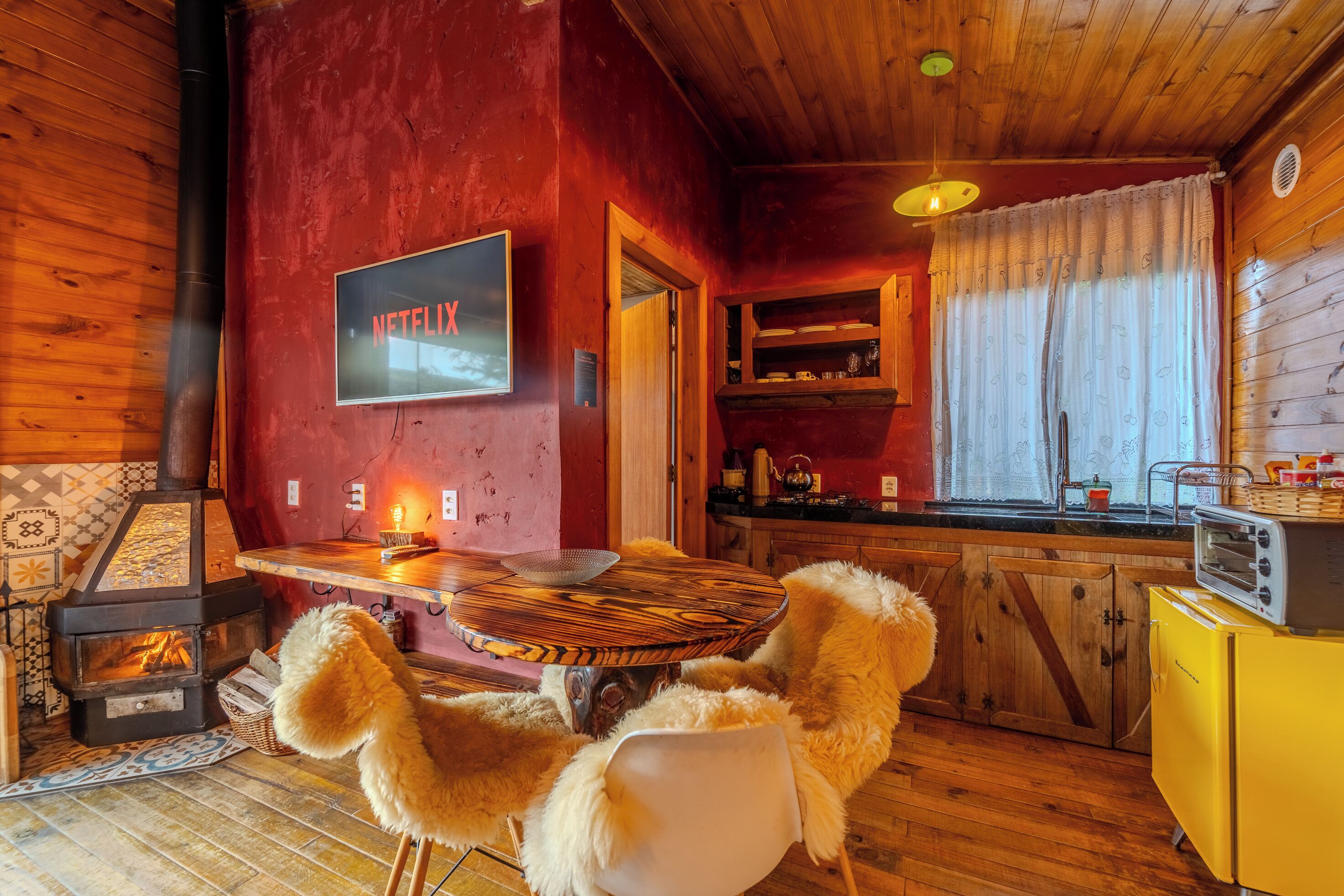 Een gezellig interieur van een chalet met een houten eettafel, een televisie aan de muur, een keuken met een gele koelkast, en een open haard.