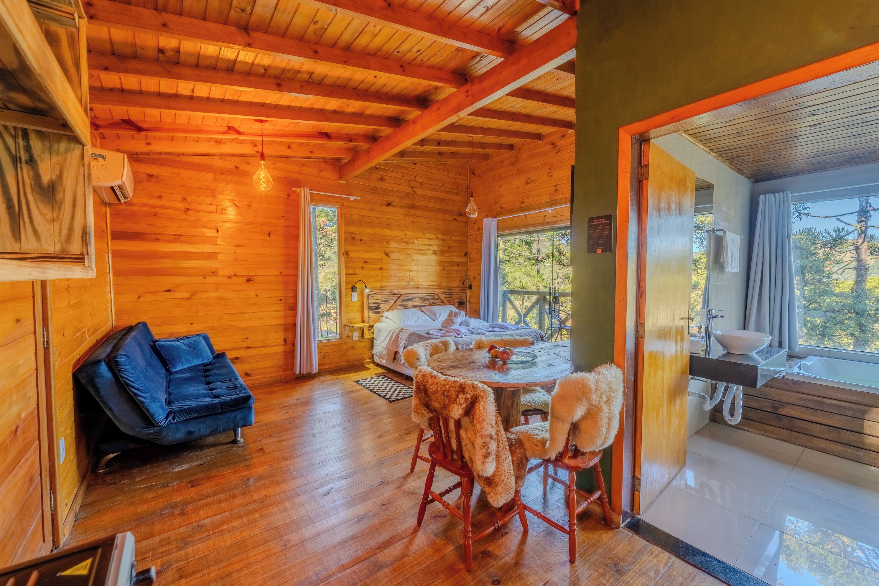 A wooden cabin interior with a bed, a round dining table, and a sofa.
