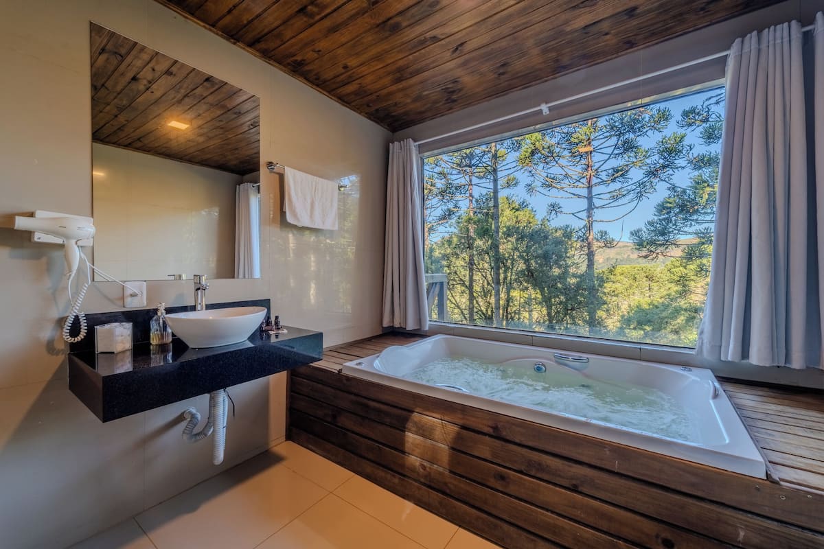 Une salle de bain moderne avec un plafond en bois, une grande fenêtre donnant sur les arbres, un lavabo avec un vasque et une baignoire sur pieds.