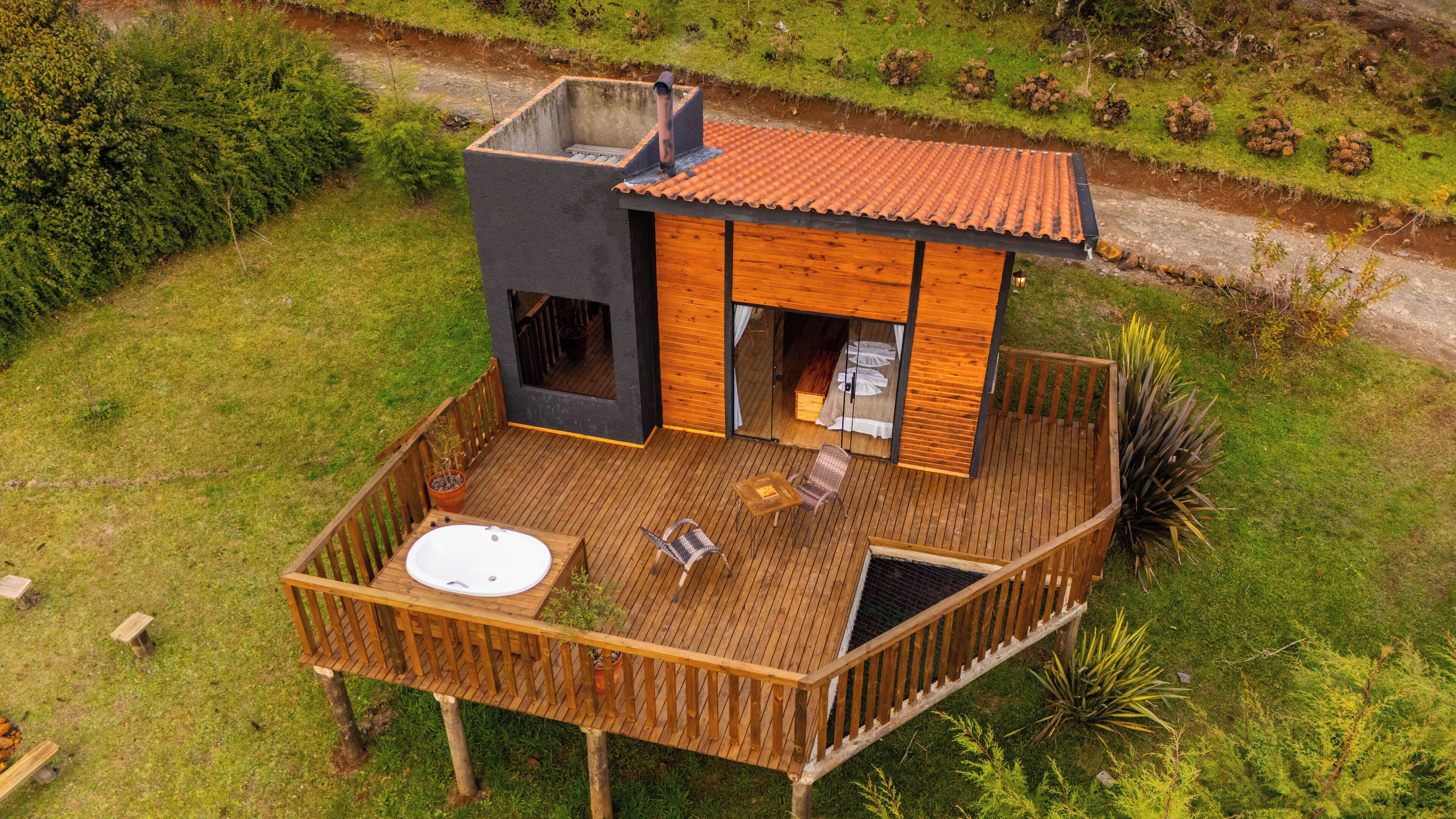 Une terrasse en bois avec un jacuzzi, des sièges et un petit bâtiment doté d’un toit recouvert de tuiles.