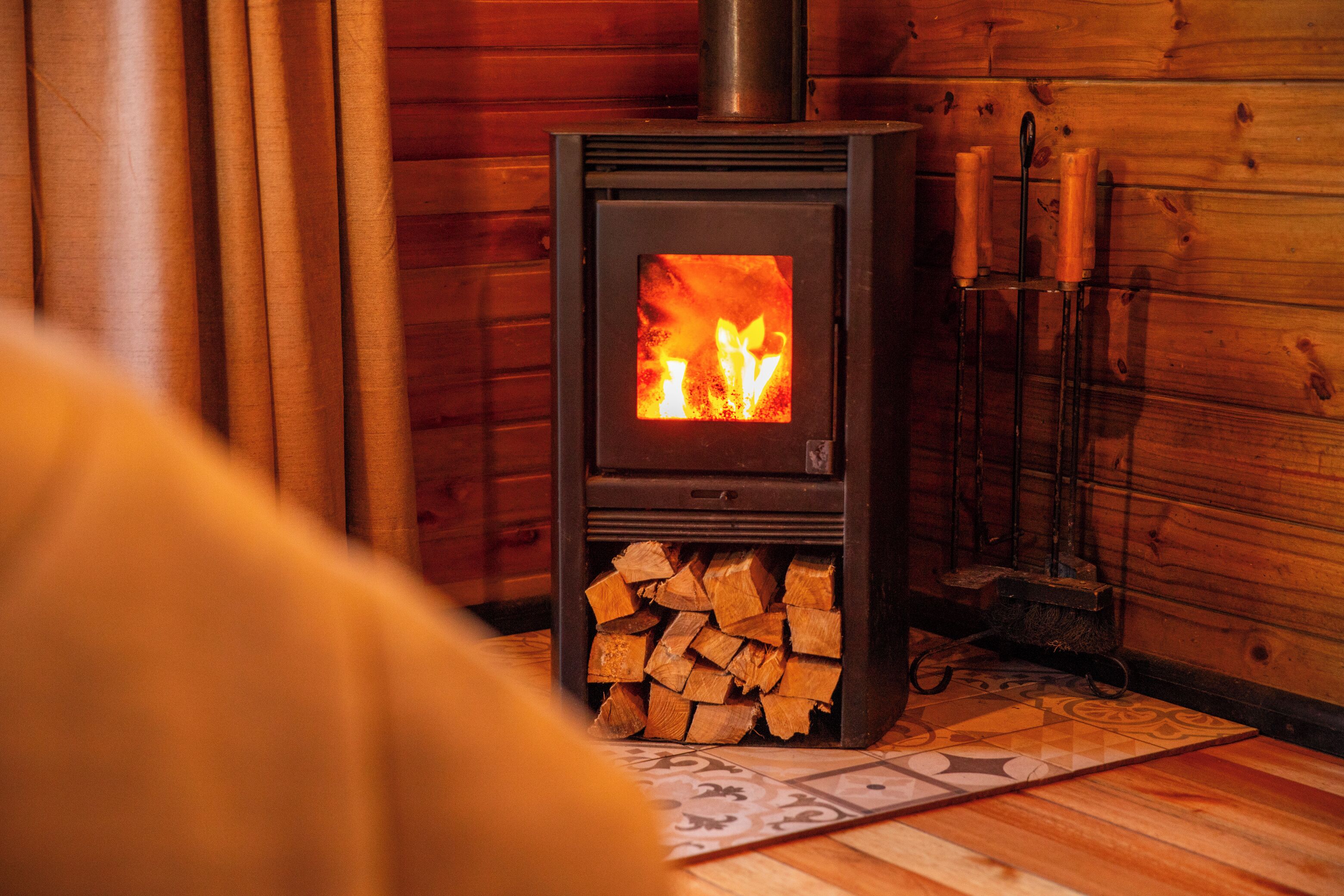 A wood-burning stove with a fire burning inside, placed against a wooden wall.