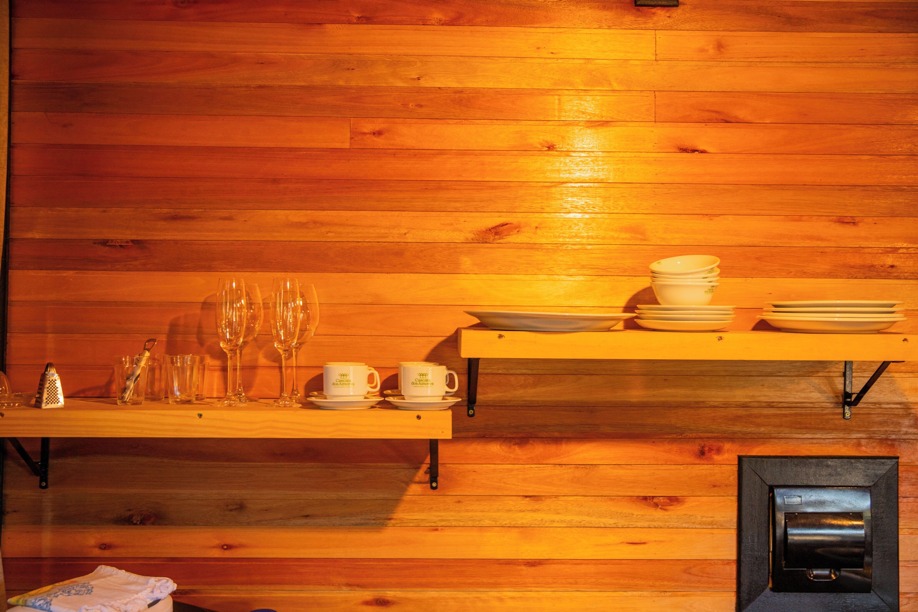A wooden interior with a shelf holding plates, cups, and glasses.