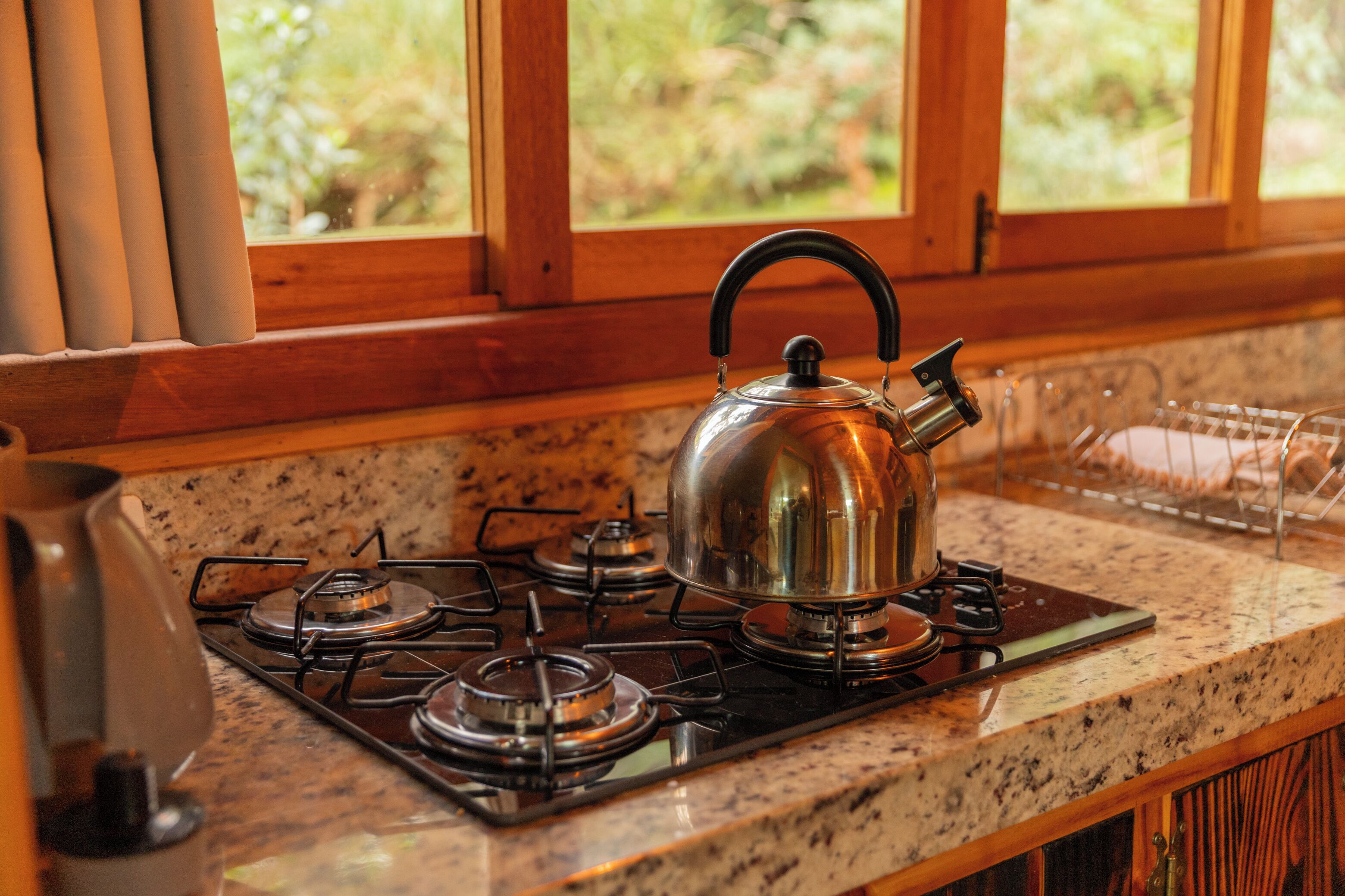 Una cocina con estufa a gas, hervidor de agua y ventana con vistas a zonas verdes.