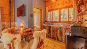 A wooden interior with a dining table, chairs, a refrigerator, and a window with a view of trees. - Cascata dos Amores (Urubici)