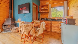 A cozy cabin interior with a wooden interior, a fireplace, a dining area with chairs, a kitchen with a sink, and a television labeled "NETFLIX". - Cascata dos Amores (Urubici)
