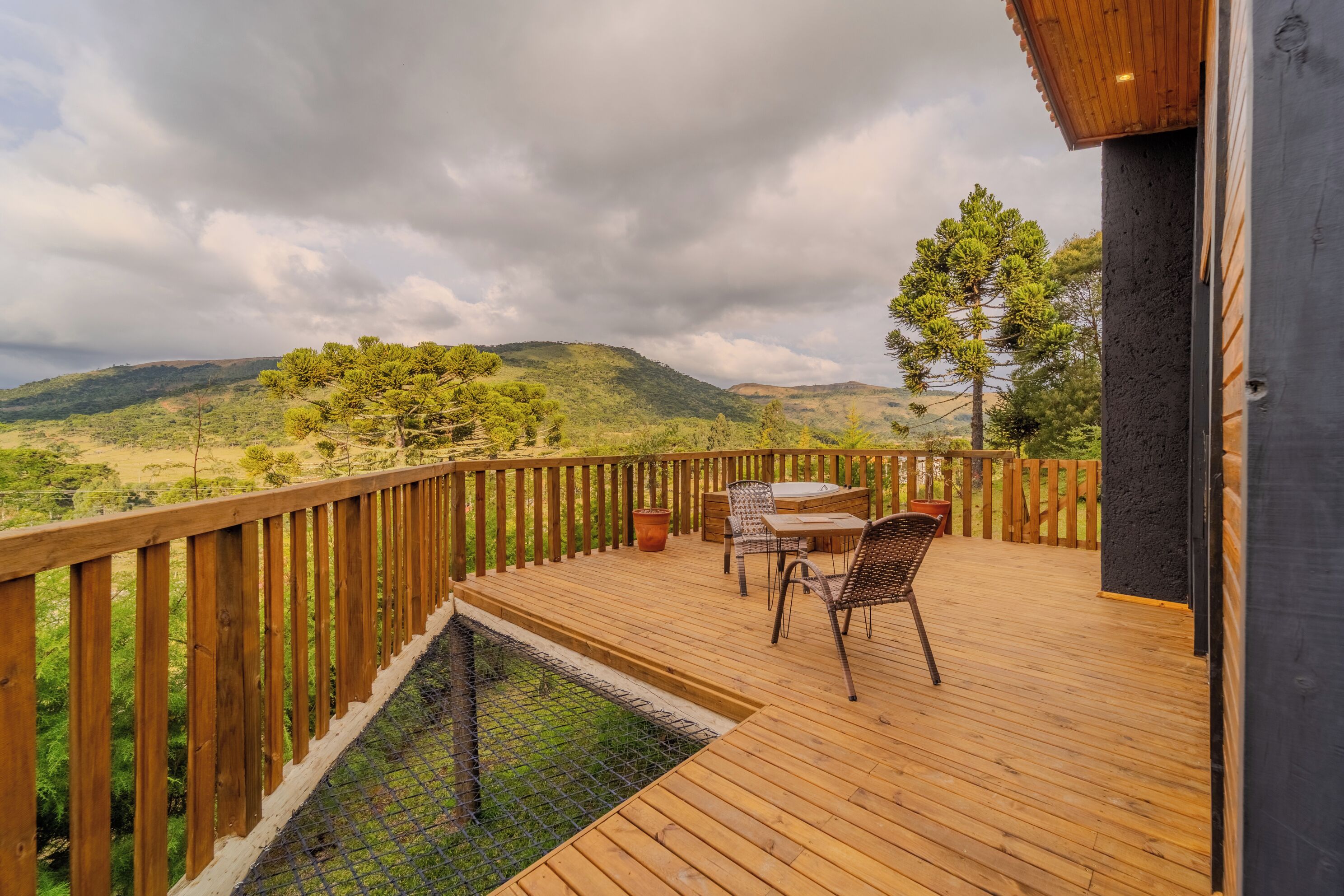 Una terraza de madera con mobiliario exterior, una piscina y vistas a un paisaje montañoso.