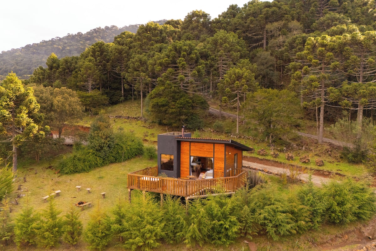 Une cabane en bois dotée d’une terrasse, entourée d’une forêt dense et de collines.