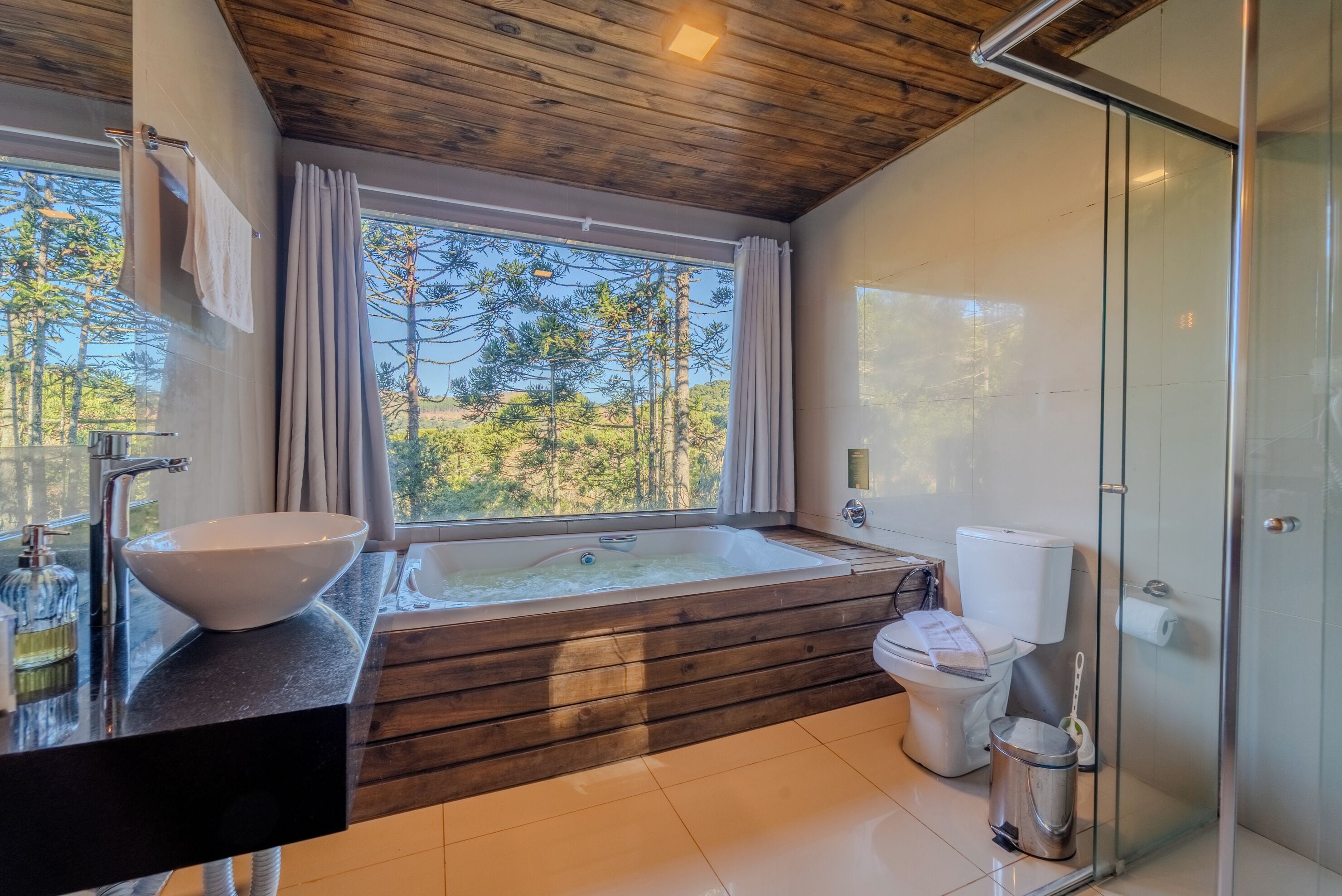 Un baño moderno con un ventanal grande, bañera de madera y mampara de cristal.