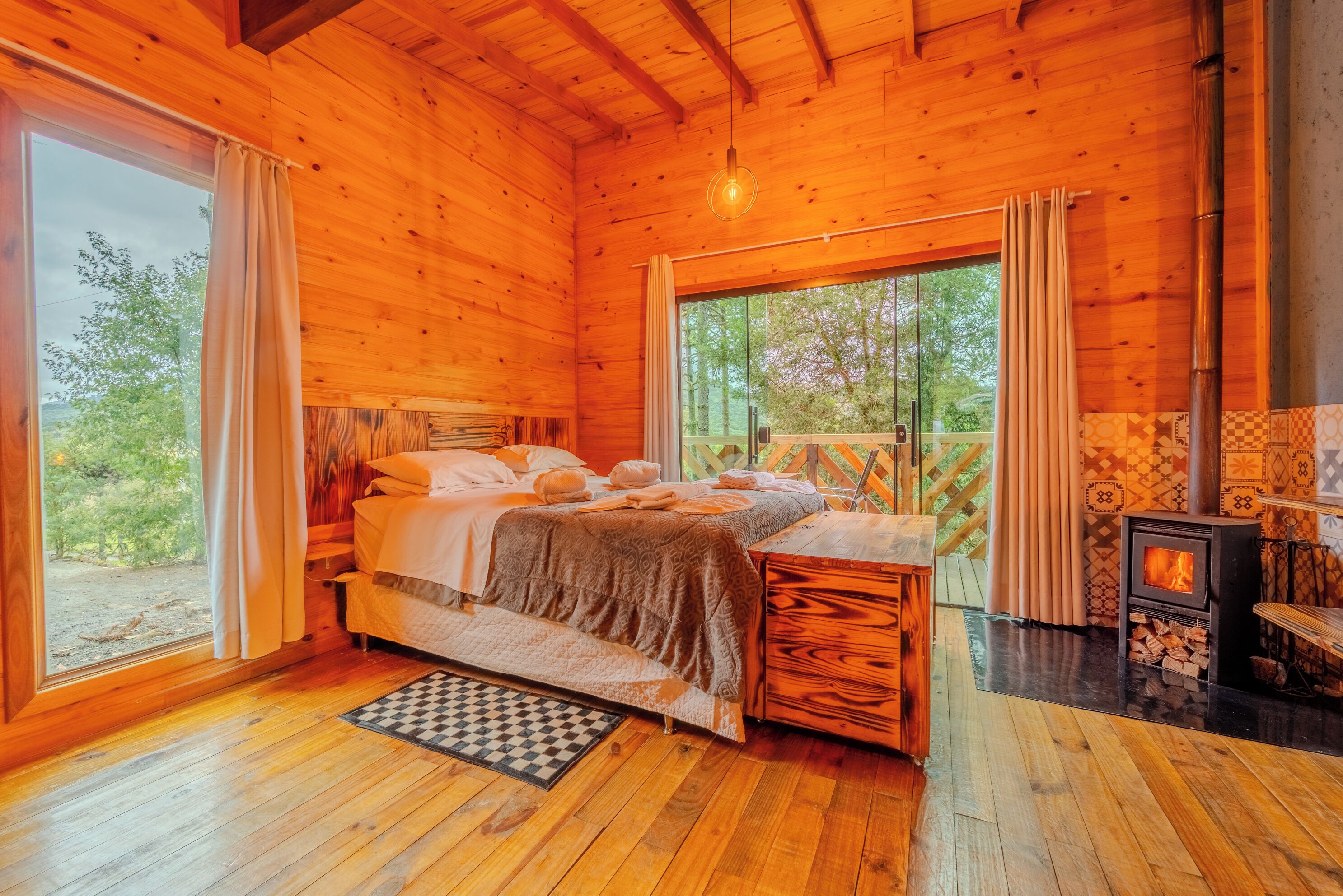 A wooden cabin bedroom with a bed, a fireplace, and a large window.