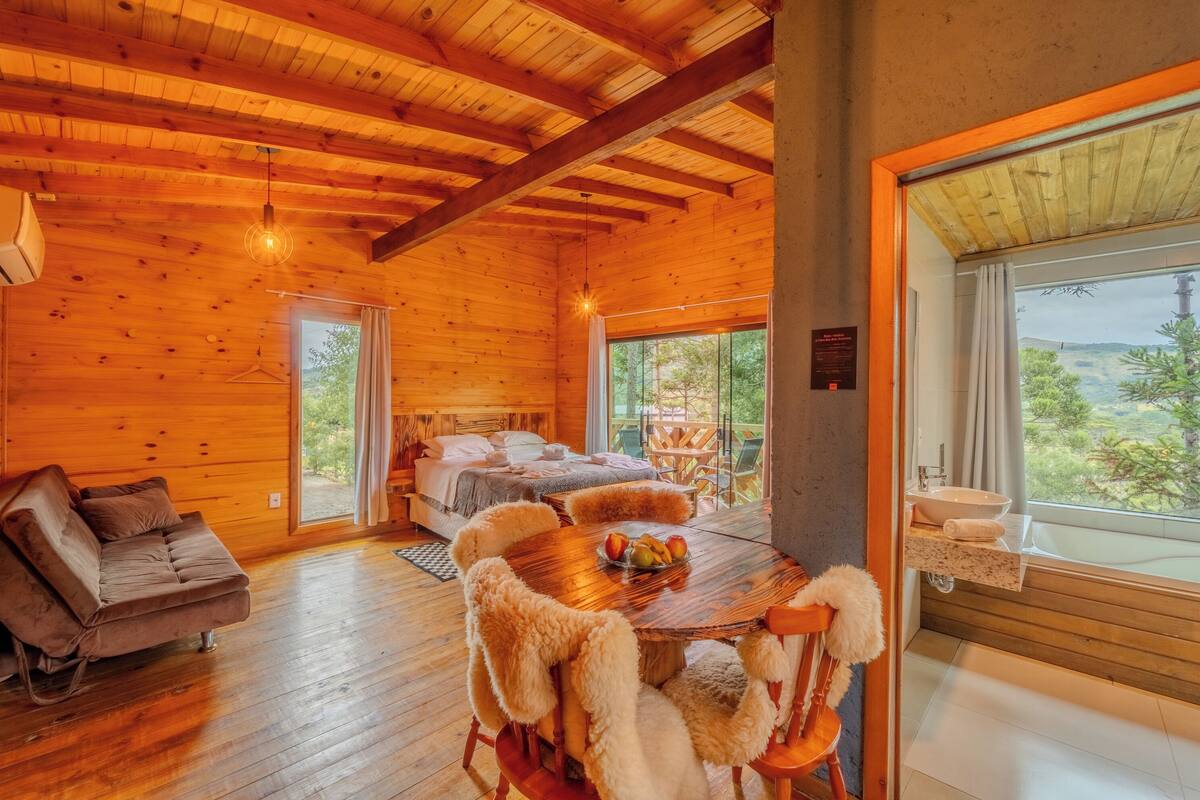 L’intérieur d’un chalet en bois comprend un lit, un canapé, une table à manger et une salle de bain dotée d’une grande fenêtre.