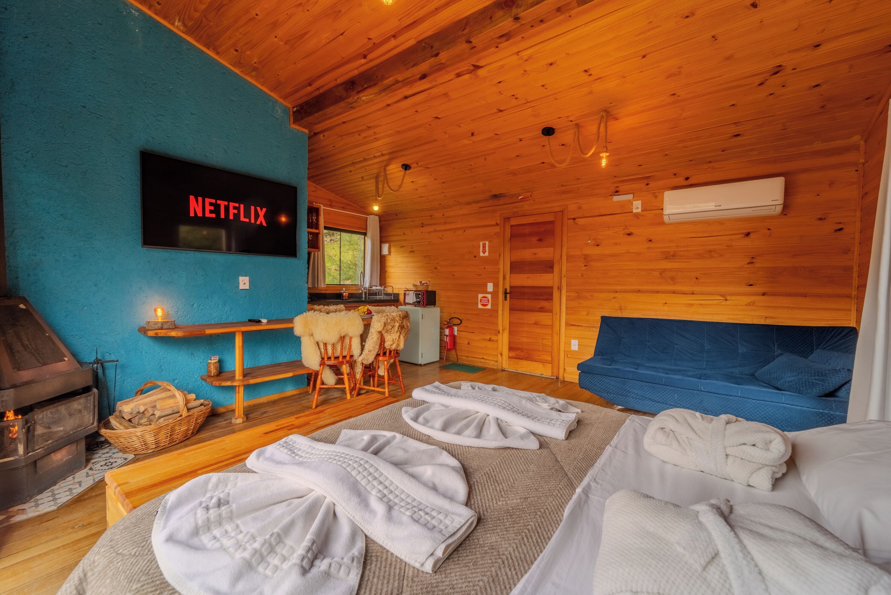 Een knus chalet met houten inrichting, een open haard, een Netflix-bord, een bank en een tafel met handdoeken.