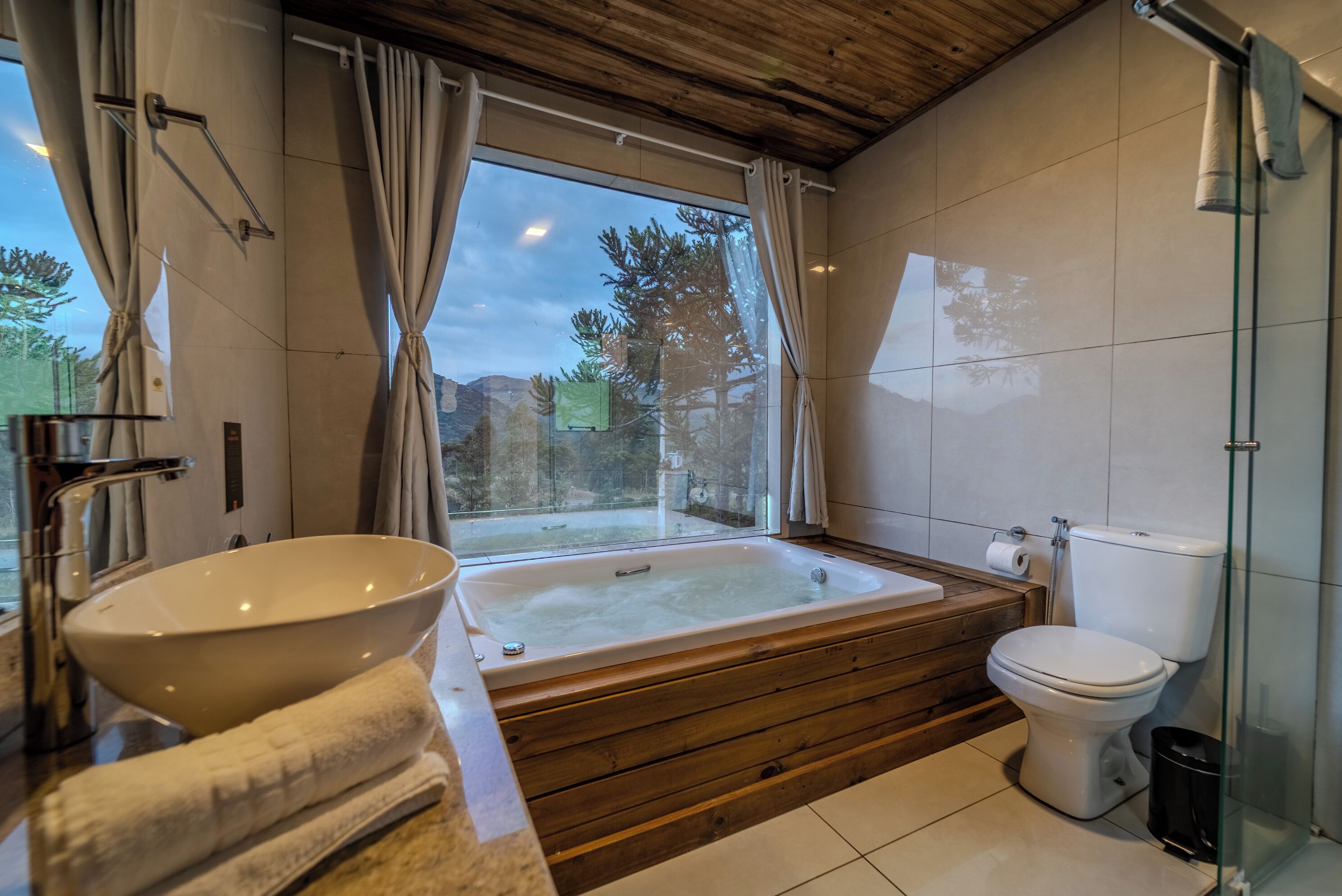 A bathroom with a bathtub, toilet, and a large window with curtains.