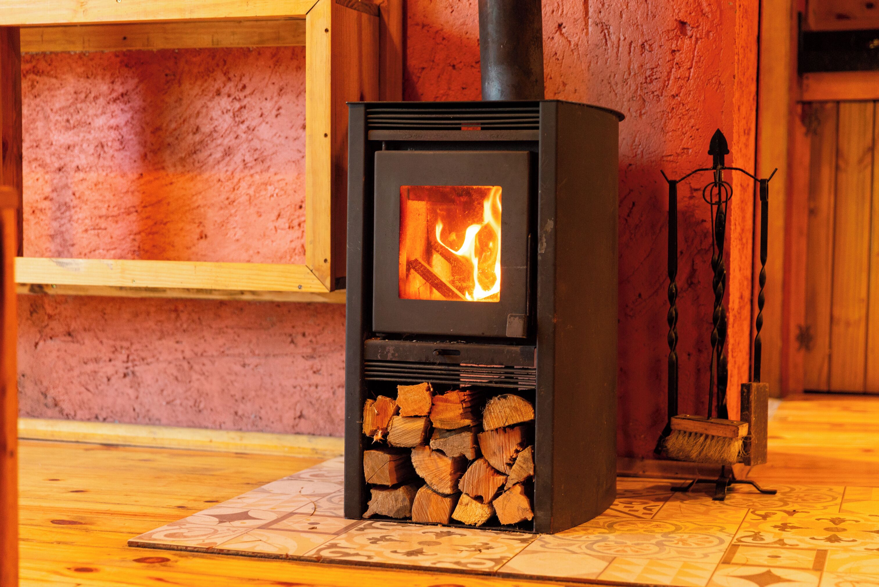 A wood-burning stove with a fire burning inside, placed on a patterned tile floor.