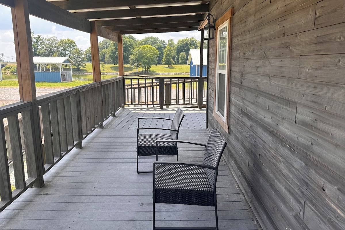 A covered porch with two black metal chairs and a wooden deck.