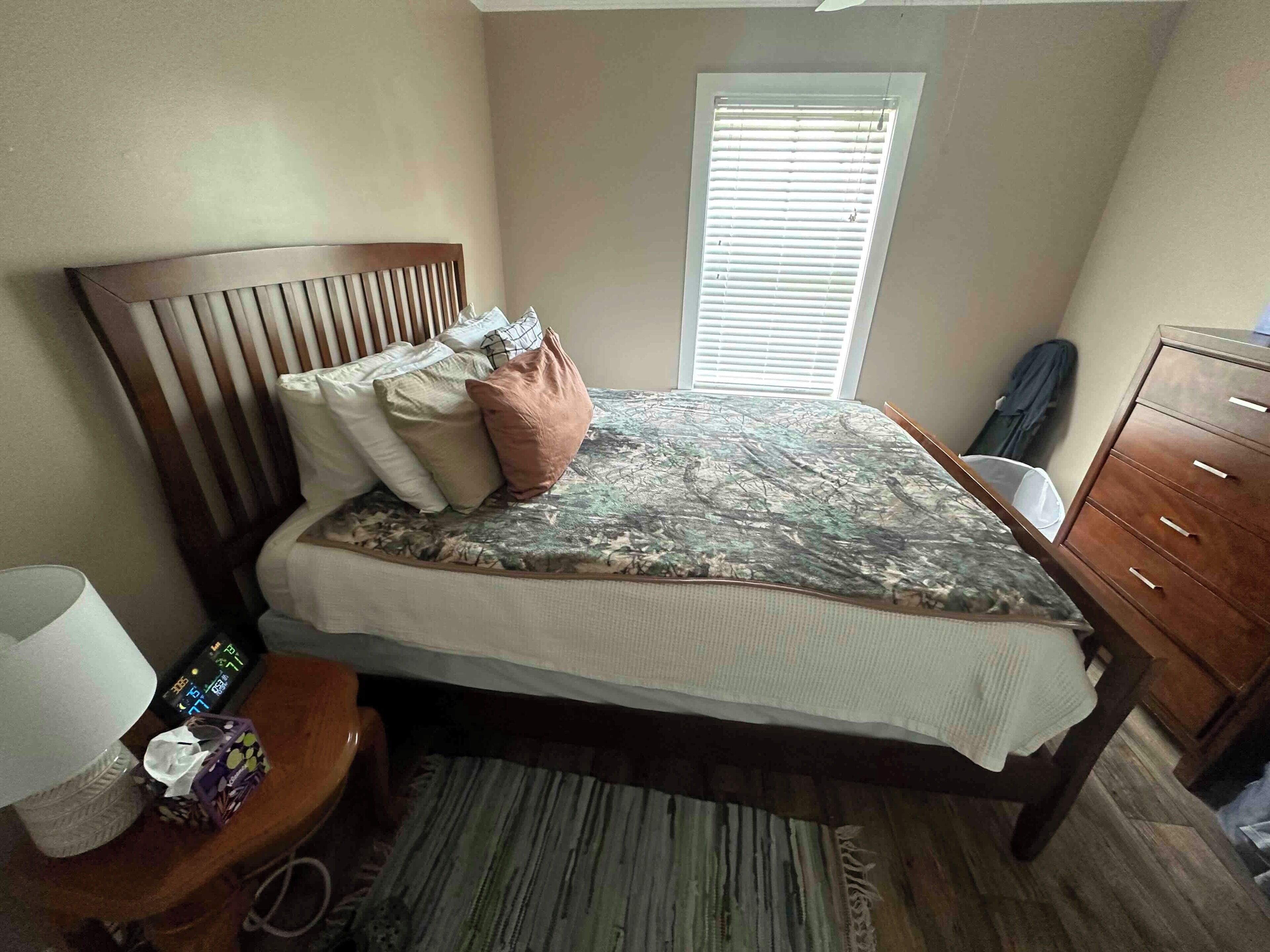 Un dormitorio con cama, mesita de noche, lámpara y ventana con persianas.