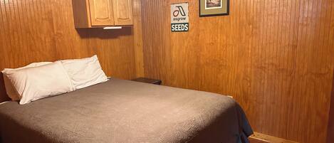 A wooden-paneled room with a bed, a ceiling fan, a framed picture, and a sign on the wall.
