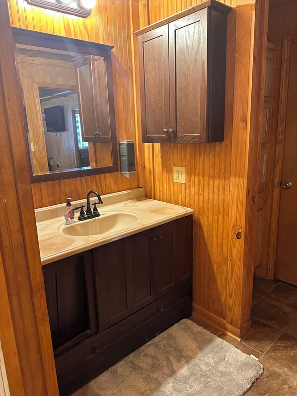 A wooden-paneled bathroom with a sink, mirror, and cabinets. - Red Leaf Cottages (Lake Village)