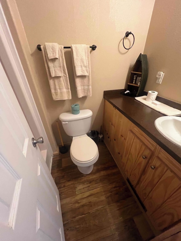 A bathroom with a toilet, a sink, and a wooden vanity. - Red Leaf Cottages (Lake Village)