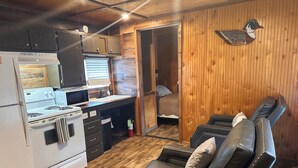 A compact kitchen with a stove, microwave, and cabinets, a dining area with a table and chairs, and a seating area with a couch. - Red Leaf Cottages (Lake Village)