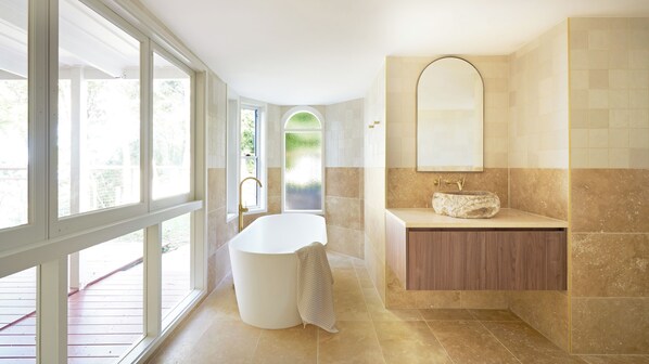 Une salle de bain moderne avec une baignoire sur pieds, un grand miroir et un meuble-lavabo avec un vasque en pierre.