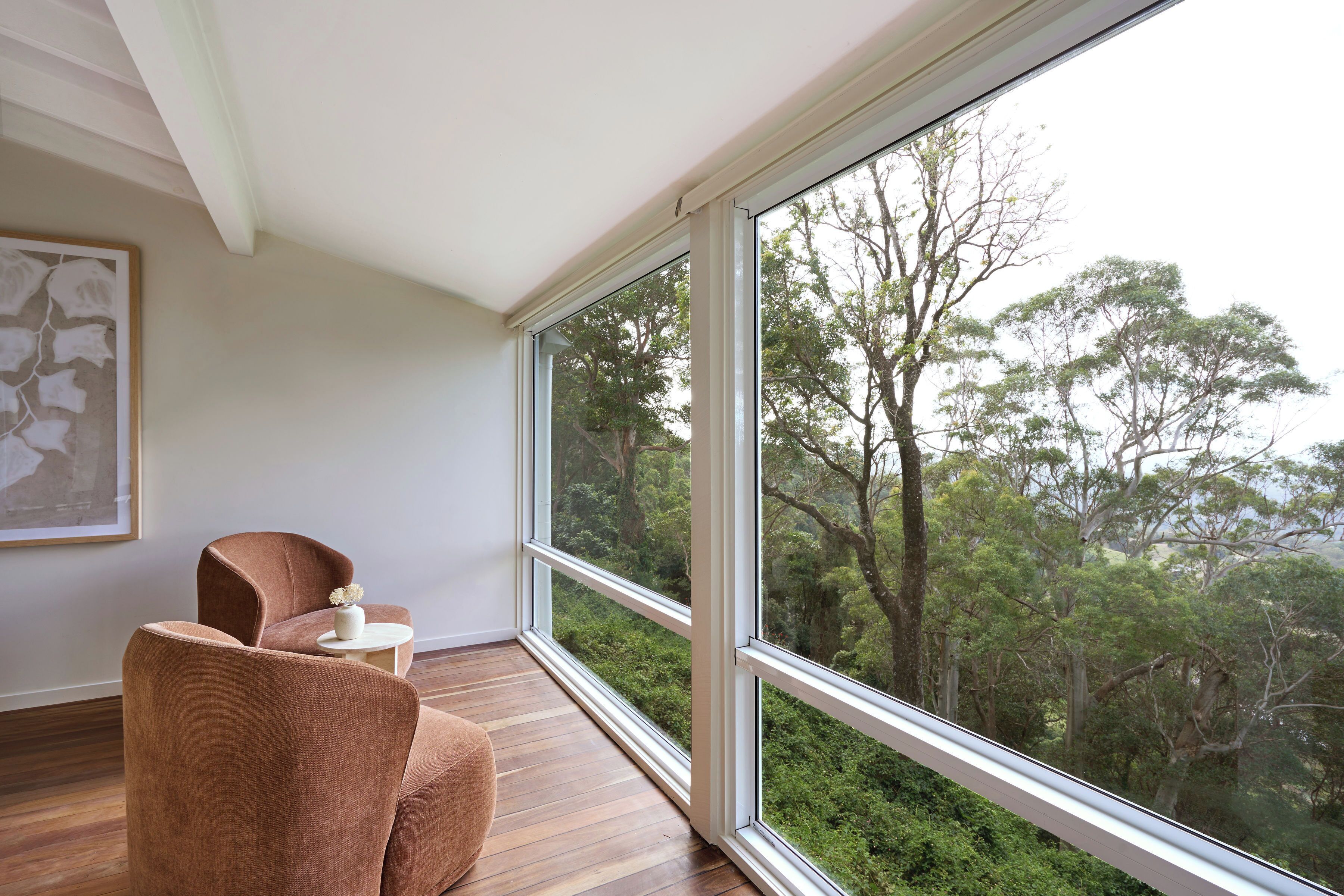 A room with a large window, a wooden floor, and two brown chairs.