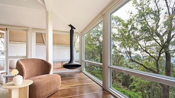 A modern room with a large window, a brown chair, a round wooden table, and a black hanging light fixture.