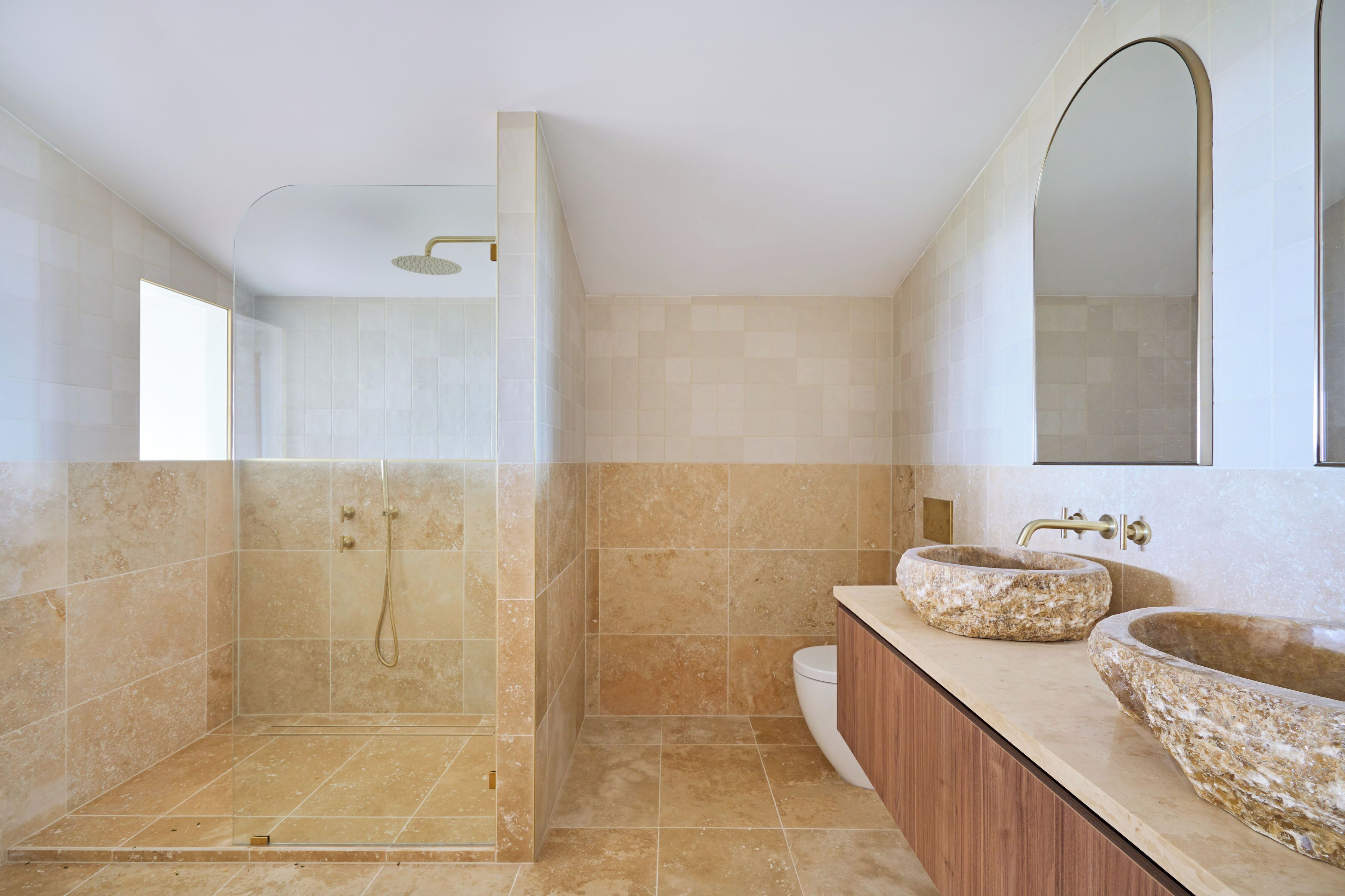 A modern bathroom with a glass-enclosed shower, two stone sinks, and a large mirror.