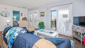 A living room with a sofa, armchair, coffee table, TV, and a sliding glass door to a balcony.